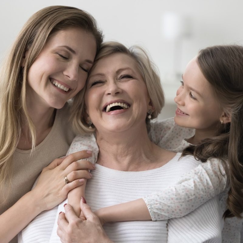 Joyful grandkid girl and adult daughter woman hugging happy excited grandma, celebrating birthday, mothers day, smiling, laughing, having fun, enjoying family meeting, warm relationships